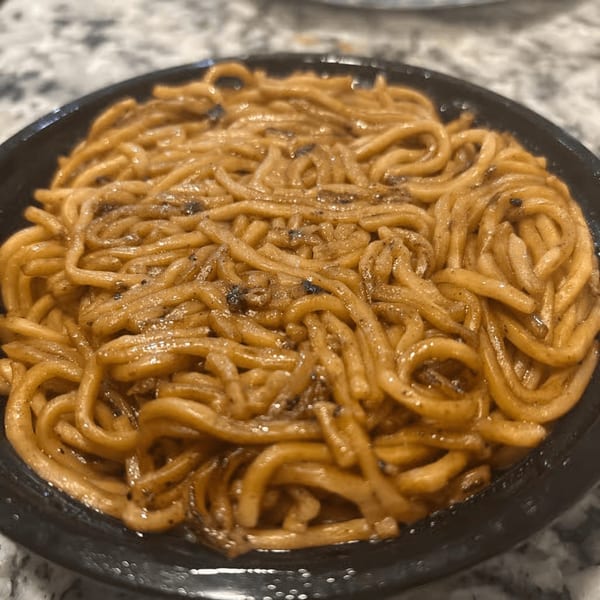 Close-up of King's Chinese restaurant's brown lo mein noodles with dark specks in a black bowl.